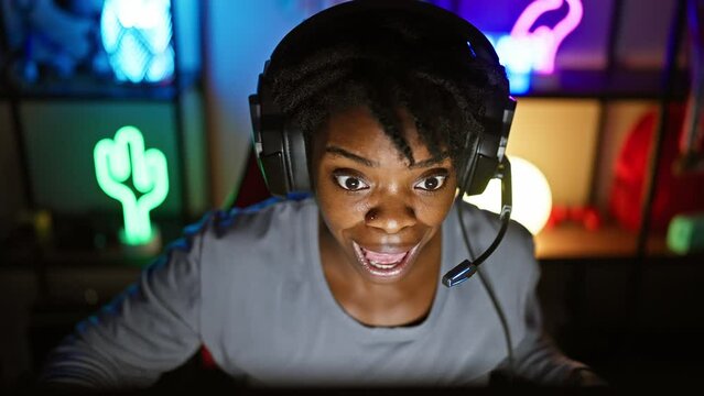 Amazed young black woman with dreadlocks, wide open mouth in surprise, playing game indoors. scared and disbelief etched on her face, gaming room full of wonder and shock.