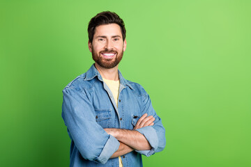 Photo of good mood charming guy dressed jeans shirt arms crossed empty space isolated green color...
