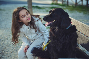 Beautiful little child girl talking to her best companion - a black young cocker spaniel dog,...