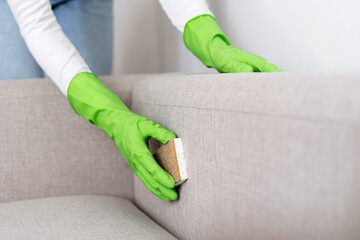 Selective focus on female hands in gloves washing sofa upholstery with sponge