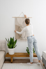 Woman hangs macrame on the wall in living room