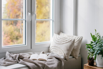 Home interior with cozy windowsill with blanket, cushions and paper book in room
