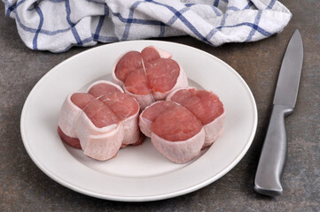 Paupiettes de veau crues dans une assiette avec un couteau en gros plan.