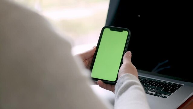 professional holding a smartphone with a green screen, ready for digital customization. Positioned next to a laptop in a work setting software applications, mobile technology demonstrations