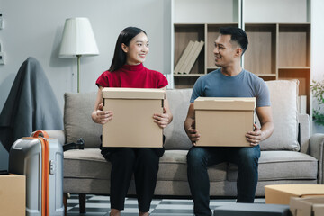 Young couple relaxing sitting on the floor around cardboard boxes at home, smiling happy moving to a new house.