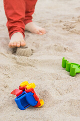 Little car, children toys and feet of little boy. Relax or playing on sand at beach. Summer and vacation time