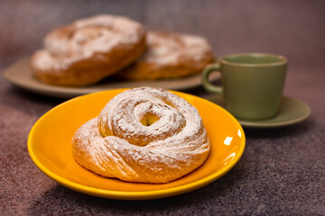 An ensaimada on a yellow plate with other ensaimadas and a cup in the background