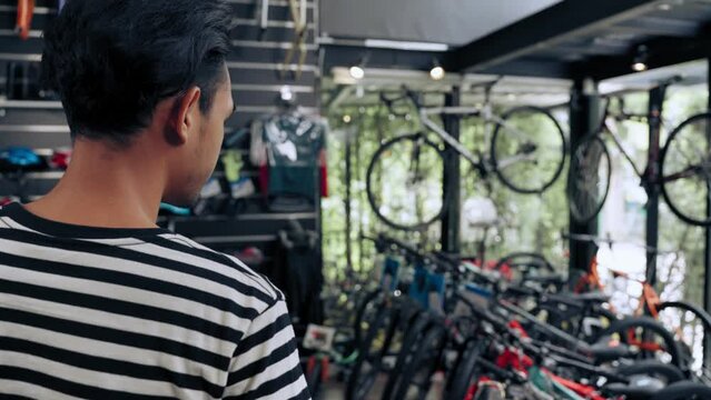Young Asian man selection and deciding purchase new bicycle in bicycle shop, Consumerism concept