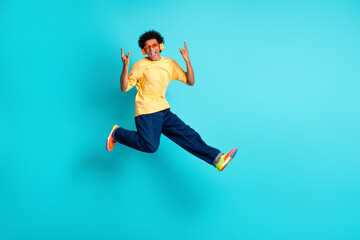 Fototapeta premium Full size photo of attractive brutal man wear oversize t-shirt denim pants jumping show rock symbol isolated on teal color background