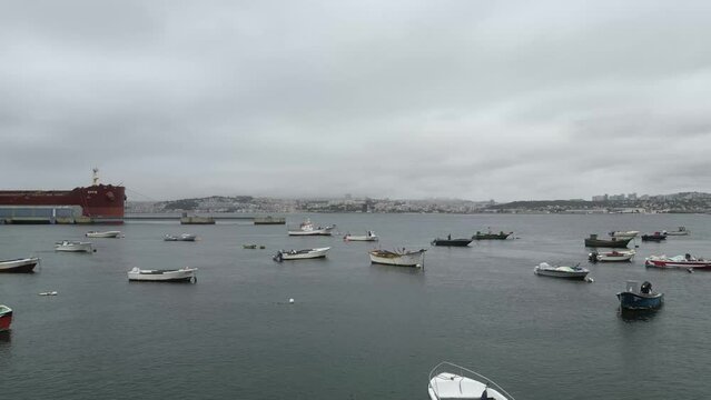 Spectacular drone footage of Trafaria Silopor Harbor captures vibrant maritime activity. Cargo ships unload against the charming coastal town backdrop. Perfect for travel and maritime projects.