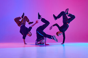 Energetic photo of talented boys, in black attire performing hip-hop in motion in mixed neo n light against vibrant gradient background. Concept of sport and hobby, music, fashion and art, movement. © Lustre Art Group 