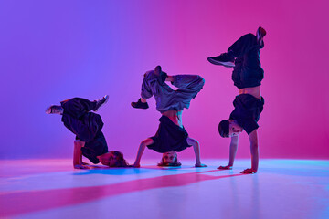 Dynamic photo of talented boys, in black attire performing hip-hop in motion in mixed neon light...