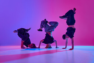 Fototapeta premium Dynamic photo of talented boys, in black attire performing hip-hop in motion in mixed neon light against vibrant gradient background. Concept of sport and hobby, music, fashion and art, movement. Ad