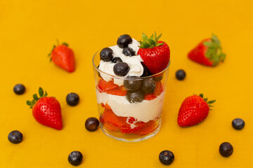 strawberry and blueberry dessert with whipped cream in a glass on yellow background