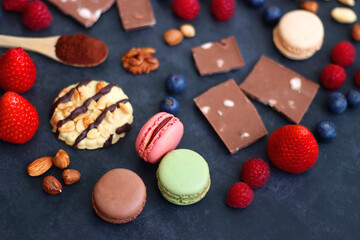 Macarons, chocolate, cookies, berries and various nuts on dark blue background. Selective focus.