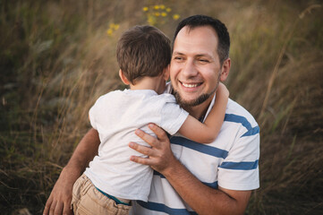 Father and son hug in front of a field. A happy dad hugs his little son against the backdrop of the sunset. Father's day holiday