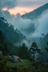 Tent on a hillside with a dramatic view of misty mountains and a colorful sunrise in the background