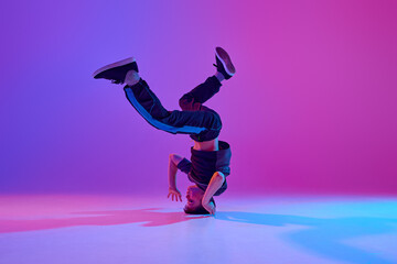 Athletic teenager, break-dancer spinning on head in motion in mixed neon light against vibrant...