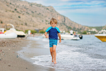 Adorable little blond kid boy running on ocean beach. Child having fun near sea. Vacations, summer, travel concept. Summer family vacations on Mediterranean Sea