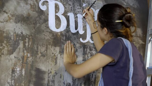 talented artist doing lettering on a mural, painting with a paintbrush