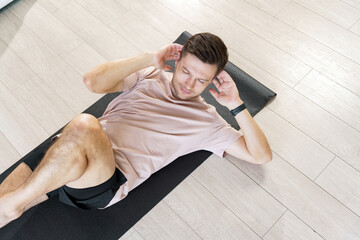 A man performs abdominal crunches on a yoga mat, displaying dedication to his fitness regimen within a modern, light-filled living space.
