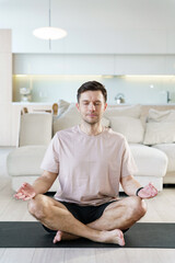 A portrait of a man deeply immersed in meditation, seated cross-legged on a yoga mat, with his eyes closed and hands in a mudra, in a serene and well-lit modern living space.