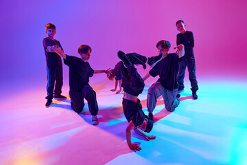 Team of young dancers in a choreographed pose, blending agility and artistry in mixed neon light against vibrant gradient background. Concept of sport and hobby, music, fashion and art, movement. Ad
