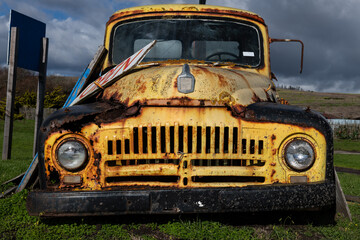 Detail view of a rusted, old, decommissioned vintage truck parked in a field of grass.