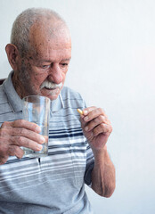 Hombre mayor anciano tomando su medicina y un vaso de agua en casa. Fondo blanco. 