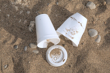 Discarded plastic coffee cups and lis lying in the sand