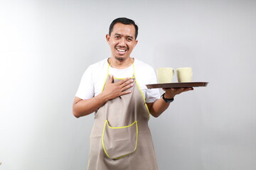 Friendly relieved barista in brown apron giving takeaway order, holding two cups of coffee and smiling, standing over gray background