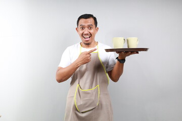 Friendly barista in black apron giving takeaway order, holding and pointing on two cups of coffee...