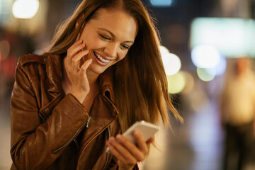 Smiling woman using smartphone at night on city street