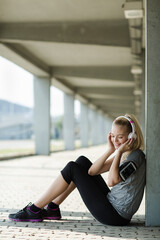Young woman relaxing with headphones after workout under a bridge