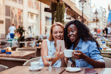 Two young women taking selfie in street cafe