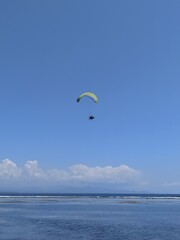 A paraglider soars in the sky above the ocean, Bali. Clear sunny day