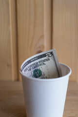 Five dollar bill in a cup on a wooden shelf, payment for coffee, tips in a cafe, donations and...