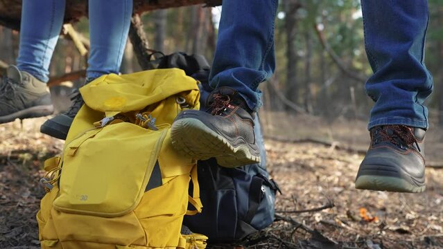 group of hikers sitting on a tree legs close-up. travel adventure lifestyle teamwork concept. tourists resting at a rest stop feet shoes close-up backpacks standing on the ground in the forest