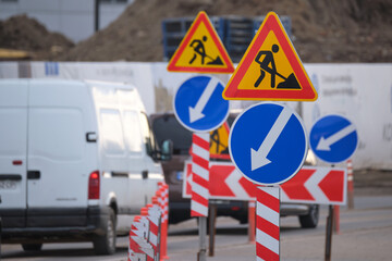 Roadworks warning traffic signs of construction work on city street and slowly moving cars