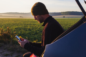 Man, traveler resting using mobile when sitting in car with spring fog Czech landscape