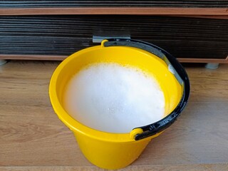 Yellow bucket with water and foam for cleaning the floor on a wooden floor. Cleaning service concept. © Natalie Dmay