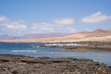 Bay and typical houses of the fishing village of Caleta de Caballo. White houses. Rock coast in the foreground. Turquoise water. Calm sea. Caleta de Caballo, Lanzarote, Canary Islands, Spain