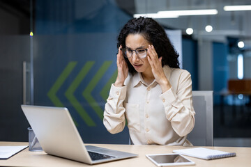 Frustrated business woman looking at laptop screen, dissatisfied female worker spreading hands inside office, latin american woman working at desk using computer for video call online communication .