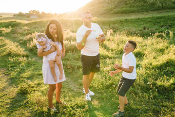 Happy family in evening sunlight. The daughter, son, and parents walk on green and yellow grass and...