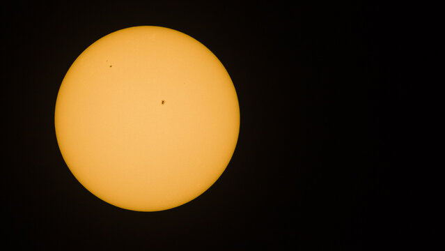 Color photo showing the full sun with a few visible sunspots against a black sky background with copy space.