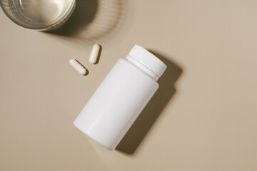 White mockup jar of pills and glass of water on beige isolated background. Concept of pharmacy, medicine, health care, daily intake of medicines and vitamins.