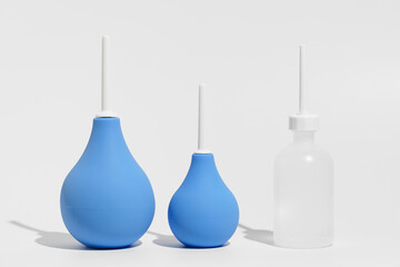 Blue rubber enemas and transparent enema filled with water on gray isolated background. The concept of medical and pharmaceutical preparations, products for cleansing the body.
