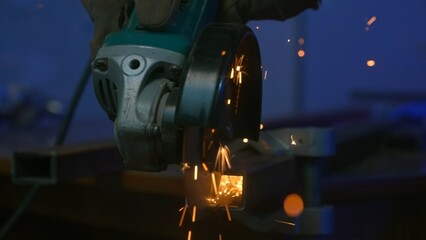 Craftsman working with grinder at industrial plant, man grinding iron detail, sparks flying around...