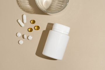 Yellow and white pill capsules and white pill jar mockup on beige isolated background with glass of...