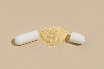 Opened capsule pill shell with powder filling on beige isolated background. Concept of natural pills, scientific medical developments and pharmacy.